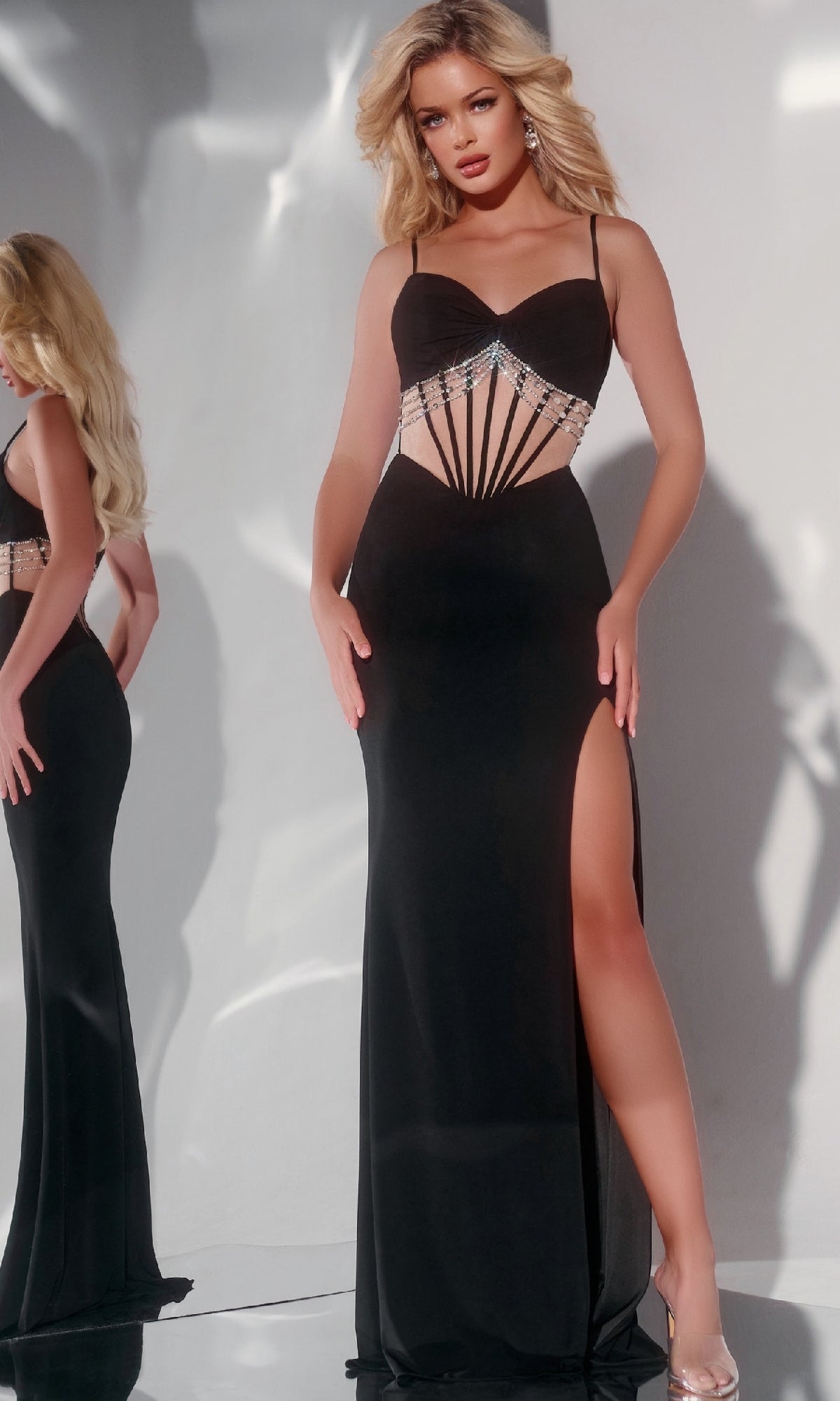 A woman poses in front of a mirror wearing the Jovani 42758 Long Prom Dress, a black evening gown featuring a high slit, sweetheart neckline, and geometric jeweled accents.